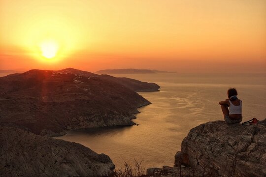 Folegandros, Greece - August 4, 2014 : A single person sitting at the top of a cliff and watching the amazing sunset of Folegandros cyclades Greece