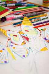 Top view of colorful, kid-drawn pictures, felt-tip pens and pencils on a white table. Creative ideas, creativity and early learning. Education concept. Selective focus