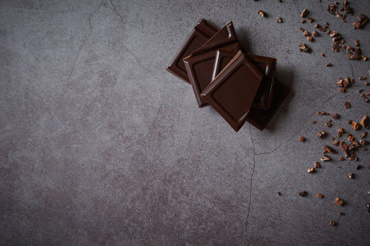 Pieces of dark chocolate with raw cacao nibs on dark stone background. High quality chocolate bar treat. Side border from top view. Empty space for text. Copy space. 