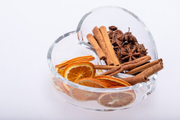Slices of dried oranges, cinnamon and cardamom in a heart-shaped glass dish