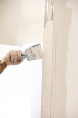 Builder using a trowel to add plaster. Plastering wall with putty-knife, close up image. Fixing...
