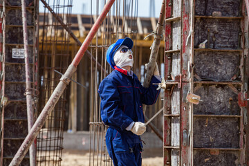 Aktau, Kazakhstan - May 19, 2012 Construction of modern asphaltic bitumen plant. Worker in white balaclava mask, and blue helmet assembling forms for pouring. Reinforcement steel on background.