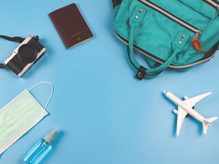 flat lay of traveling accessories with airplane model and medical face mask and alcohol sanitizer spray  on blue background. Traveling during covid-19 epidemic.