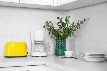 Modern yellow toaster, coffeemaker and dishware on countertop in kitchen