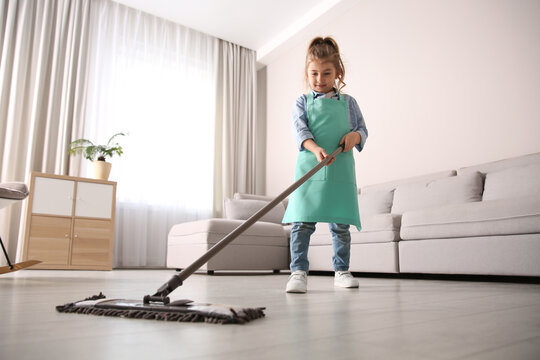 Little girl mopping floor in living room at home
