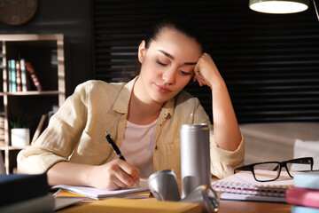 Tired young woman with energy drink studying at home
