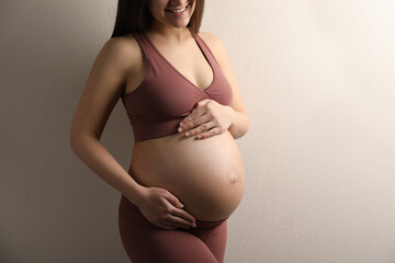 Pregnant young woman touching belly on beige background, closeup