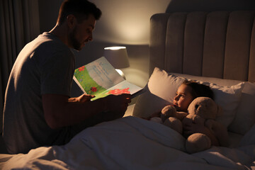 Father reading bedtime story to his daughter at home