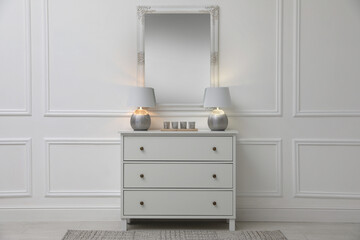 White chest of drawers with lamps near mirror in room. Interior design