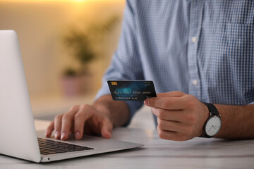 Man using laptop and credit card for online payment at table indoors, closeup