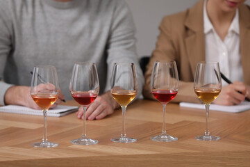Different sorts of wine in glasses prepared for tasting and sommeliers at wooden table indoors, closeup