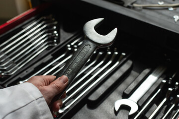 Hand of a caucasian man holding a wrench with a set of wrenches in the background