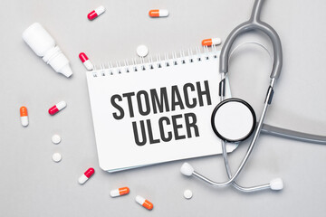 In the notebook is the text STOMACH ULCER next to a stethoscope, pills and glasses.