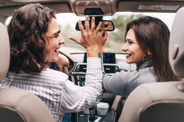 Cheerful smiling young couple in the car in front dancing to music, a pleasant ride in the car