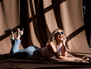Front view of beautiful woman lying on the floor covered beige fabric and having fun.