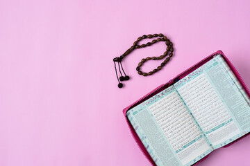 Kota Bangun, Indonesia. March 29, 2021. Top View Flatlay of Muslim Holy Qur'an and prayer beads on pink background color