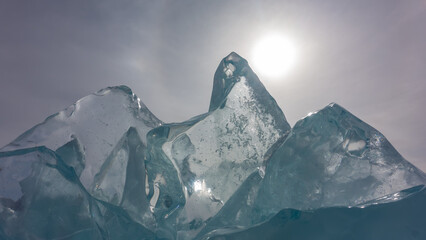 Large transparent turquoise ice floes against the sky. The sun is peeping out over the edge. A...