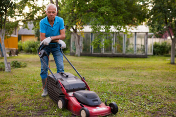 Positive elderly man with lawnmower when mowing the lawn