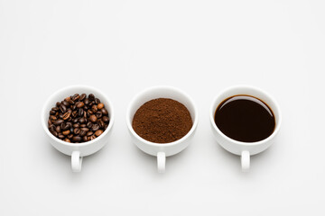 cups with prepared and ground coffee near beans on white