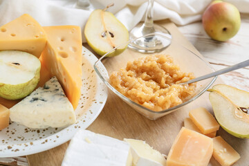 Tasty pear jam with different cheeses on table