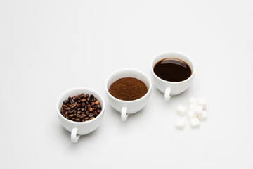 cups with prepared and ground coffee near beans and sugar cubes on white