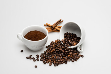 cinnamon sticks near cups with ground coffee and beans on white