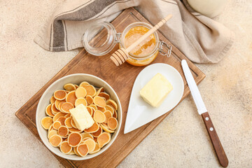 Bowl with tasty mini pancakes, butter and honey on grey background