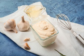 Bowl with garlic sauce and ingredients on color background