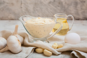 Gravy boat with garlic sauce and ingredients on grey background
