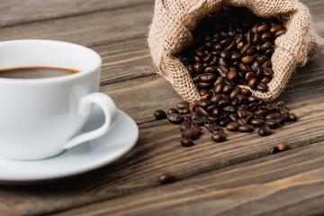 hessian sack bag with roasted coffee beans near cup on blurred foreground