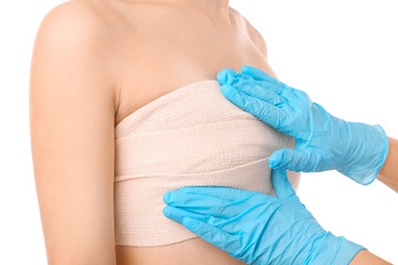 Doctor applying bandage on female chest after cosmetic surgery operation against white background