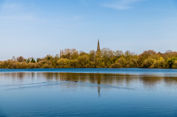 Fototapeta na wymiar A view across a lake towards the village of Attenborough on the outskirts of Nottingham, UK on a sunny spring day
