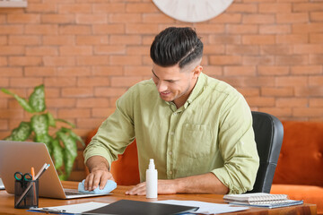 Young man cleaning laptop at home