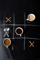 top view of tic tac toe game with spoons, cinnamon sticks and cups of coffee on black