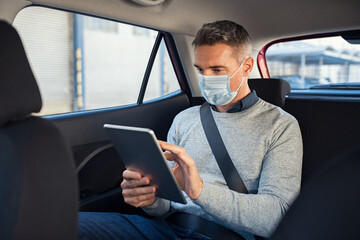 Man sitting in taxi with face mask using digital tablet