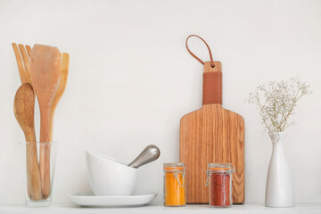 Jars with different spices, mortar and utensils on shelf in kitchen