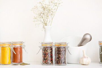 Jars with different spices and mortar on table in kitchen