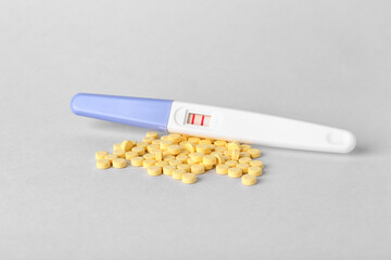 Pregnancy test and folic acid pills on light background