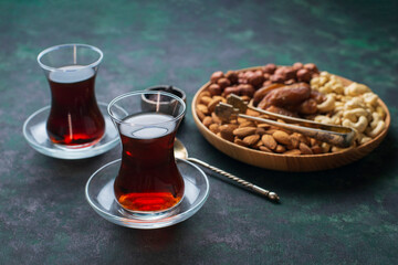 Two glasses of black strong turkish tea, platter board with nuts : cashews, almonds, dates,...