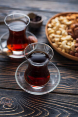 Two glasses of black strong turkish tea, platter board with nuts : cashews, almonds, dates, hazelnuts. Low sugars diet snack. Wooden plate, dark background. Slow life, Healthy tea break relax concept
