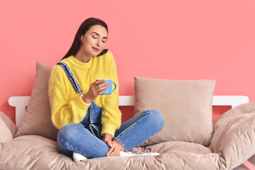 Obraz premium Beautiful young woman with cup of cocoa sitting on sofa in room