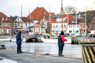 Angler mit Angelrute stehen im Hafen von Neustadt in Holstein, halten ihre Angel ins Wasser und...