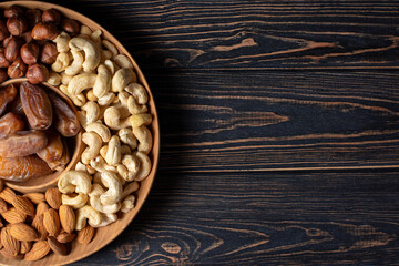 Natural organic raw nuts wooden plate on dark background top view. Platter board with healthy snack: cashews, almonds, dates, hazelnuts. Low sugars diet food. Norm of fats and oils, keto diet