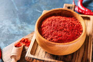 Bowl with red chili powder on color background