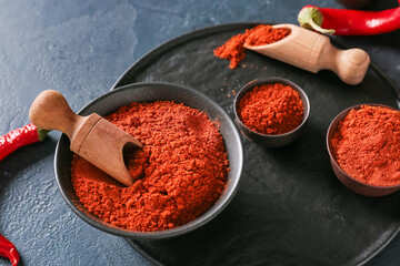 Bowls and scoops with red chili powder on dark background