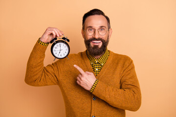 Photo of optimistic brown hair man point clock wear spectacles brown sweater isolated on beige...