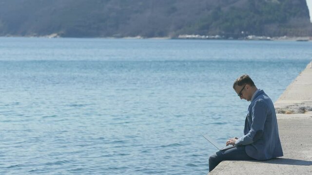freelancer businessman working remotely on laptop while sitting on the pier
