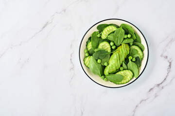 Green vegetable salad with spinach, avocado, green peas and olive oil in bowl on light gray slate, stone or concrete background. Top view with copy space. Green vegetables for diet concept.