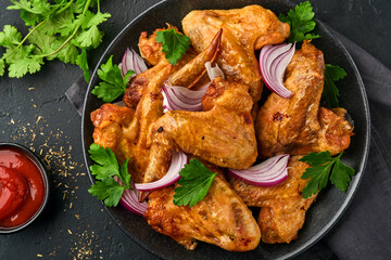 Grilled chicken wings or roasted bbq with spices and tomato salsa sauce on a black plate. Top view with copy space.