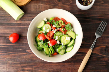 Bowl of fresh salad with vegetables on wooden background